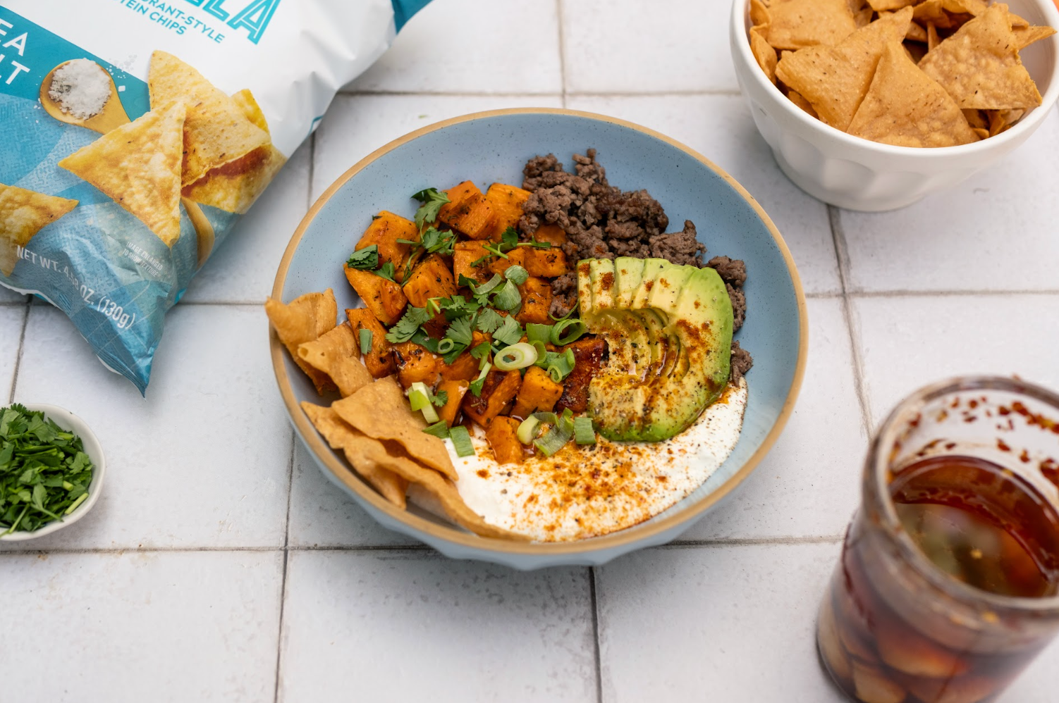  bowl of food with tortilla chips, sour cream, and avocado on a white tiled surface
