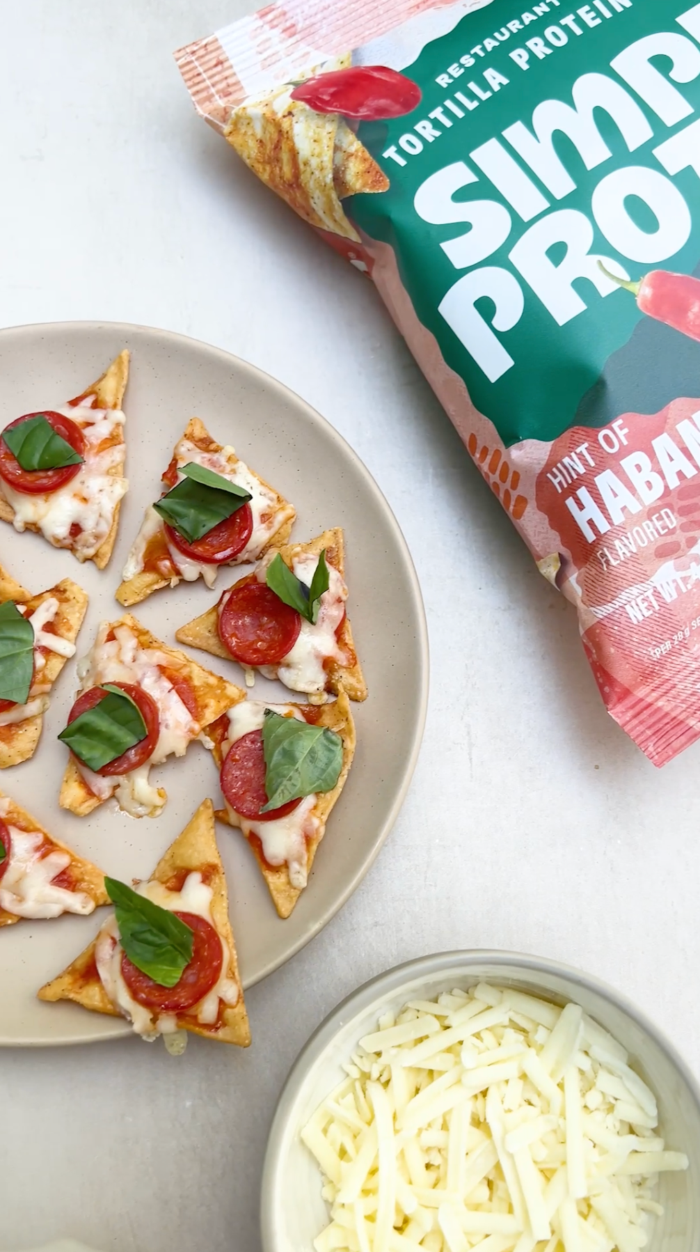 Simple Protein tortilla chips with pizza toppings on a plate, next to a package of Simple Protein Hint of Habanero flavoured chips