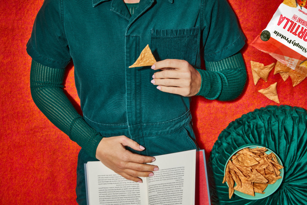Person holding a book with tortilla chips on a red background
