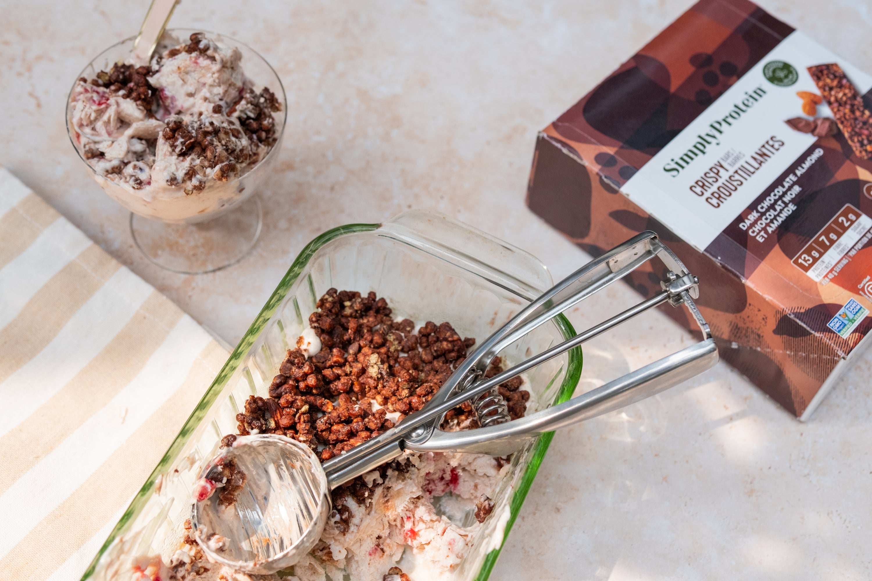 Chocolate protein ball mix with scoop, container, and dessert on a light surface